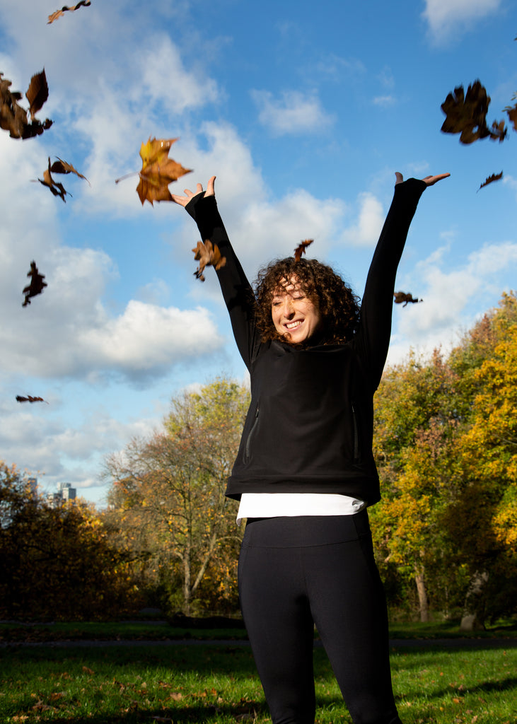 Woman wearing black sustainable jumper throwing leaves
